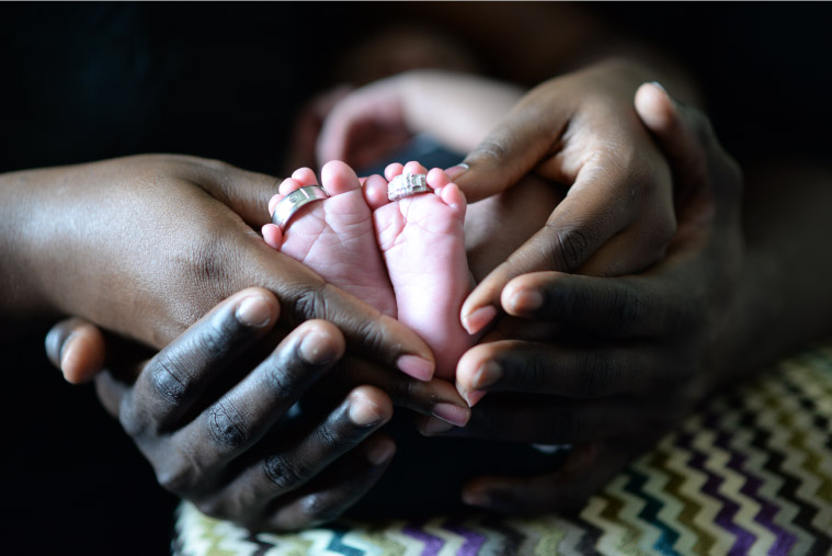 Parents hold their newborn babies feet in their hands highlighting the role of parents in early childhood development