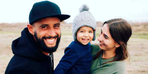 Photo of a man, a woman, and a toddler smiling at camera